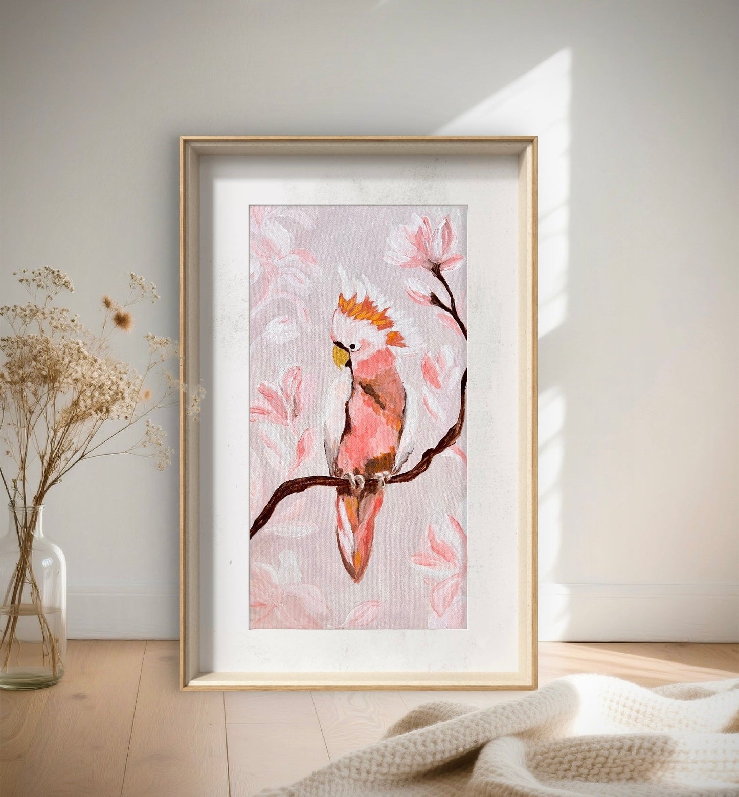 Framed artwork of a pink parrot on a branch with flowers in a minimalistic room.